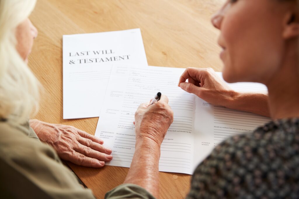 Female Friend Helping Senior Woman To Complete Last Will And Testament At Home